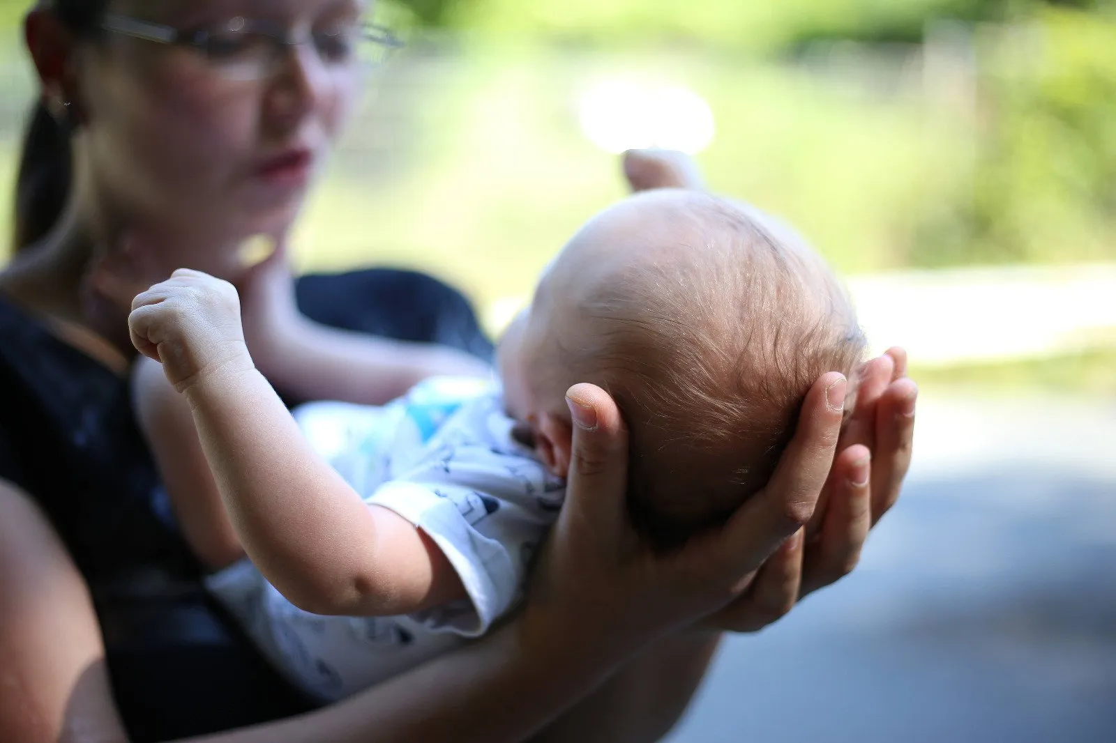 Mi Casa-Dein zu Hause - Familien- und Seniorenbetreuung - Eine Nahaufnahme mit Weichzeichner-Effekt zeigt die Hände eines Erwachsenen, die sanft den Hinterkopf eines Babys umfassen.