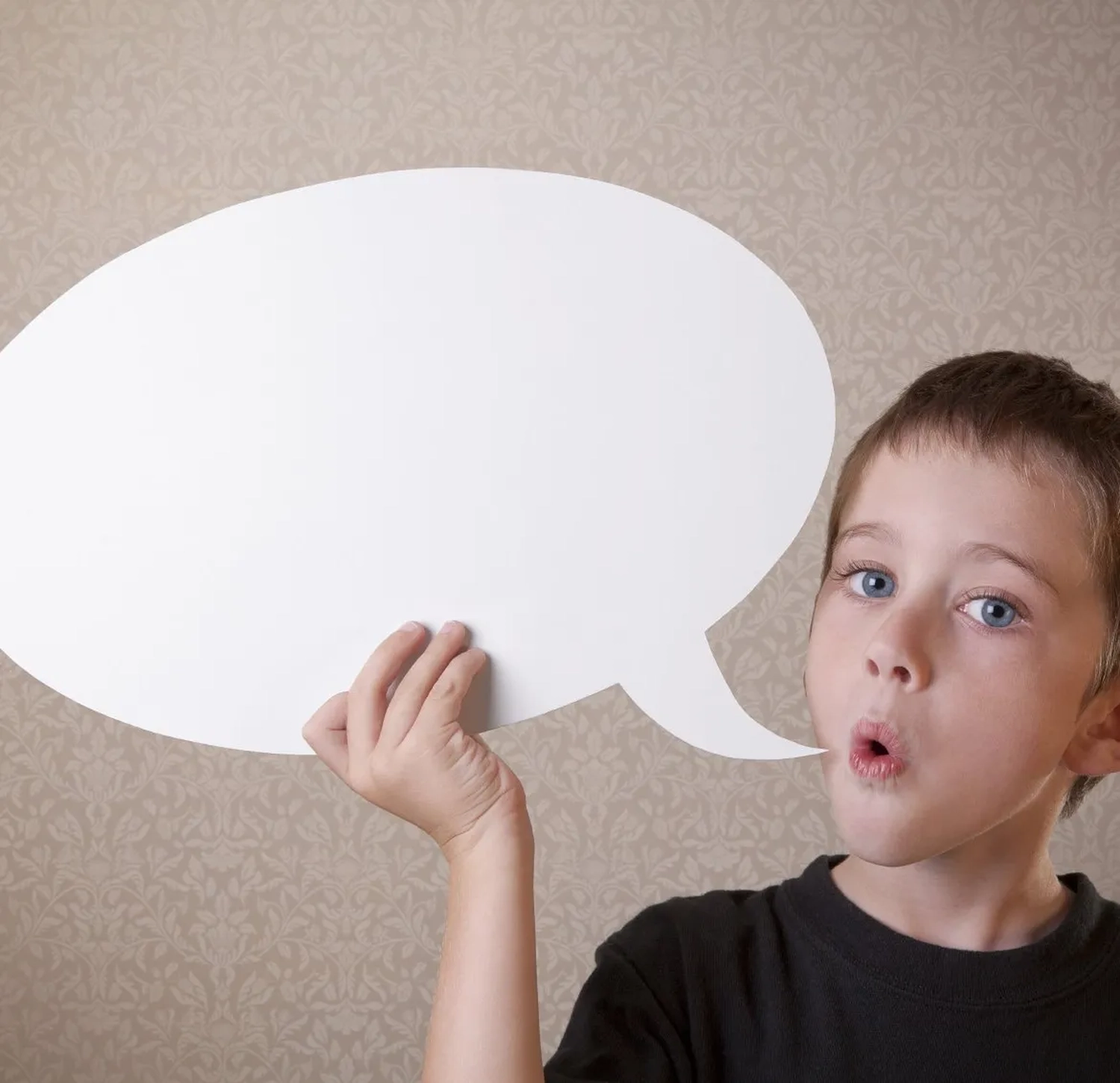 Mi Casa-Dein zu Hause - Familien- und Seniorenbetreuung - Ein Junge mit blauen Augen blickt überrascht in die Kamera, sein Mund ist zu einem „O“ geöffnet. Er hält eine große, leere weiße Sprechblase, die einen Großteil der linken Bildhälfte einnimmt.