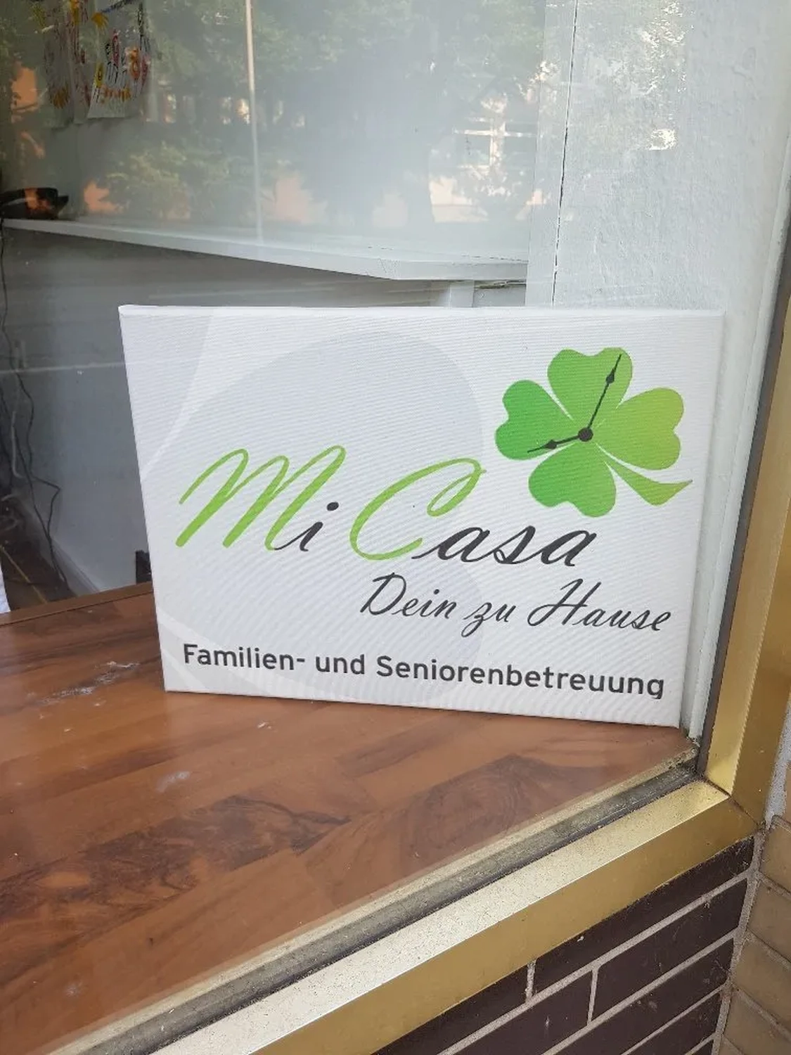 Mi Casa-Dein zu Hause - Familien- und Seniorenbetreuung - Ein Schild für „Mi Casa“, einen Familien- und Seniorenbetreuungsdienst, mit einem grünen vierblättrigen Kleeblatt als Logo.