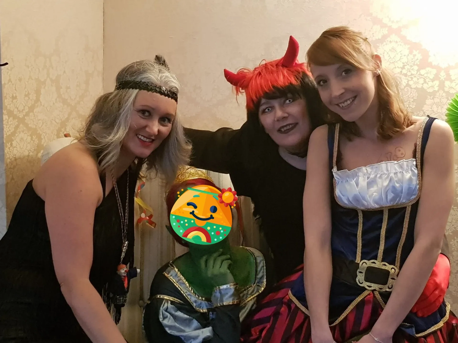 Mi Casa-Dein zu Hause - Familien- und Seniorenbetreuung - Vier Personen in verschiedenen Kostümen posieren drinnen für ein Foto. Eine Person trägt ein Stirnband, eine andere rote Teufelshörner, und eine dritte ist in einem Dirndl gekleidet. Das Gesicht einer Person ist von einem bunten Cartoon-Aufkleber verdeckt.