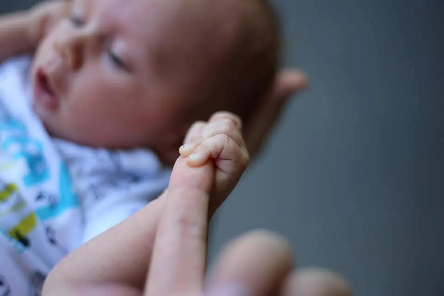Mi Casa-Dein zu Hause - Familien- und Seniorenbetreuung - Eine Nahaufnahme mit geringer Schärfentiefe zeigt die winzige Hand eines Neugeborenen, die den Zeigefinger eines Erwachsenen fest umklammert.